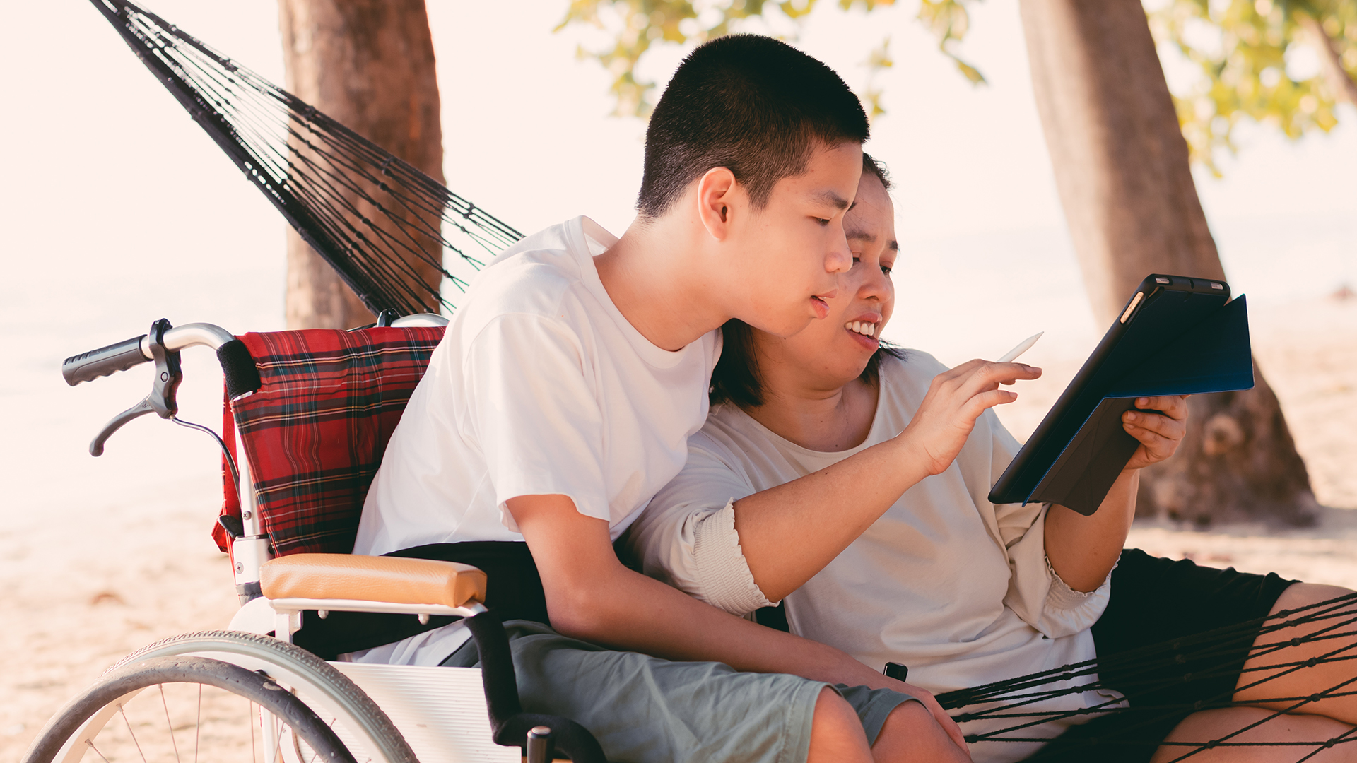 Man in wheelchair interacting with female in hammock who is using a tablet